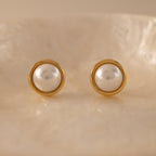 Pearl Bezel Studs in 18K Gold displayed on a light, textured surface, featuring a luminous pearl ideal for everyday wear.