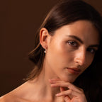 Woman with wavy brown hair wears Round Pearl Hoops in Sterling Silver, gazing thoughtfully at the camera.