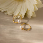 Round Pearl Hoops with delicate accents rest on a light surface near a white flower, embodying timeless jewelry elegance.