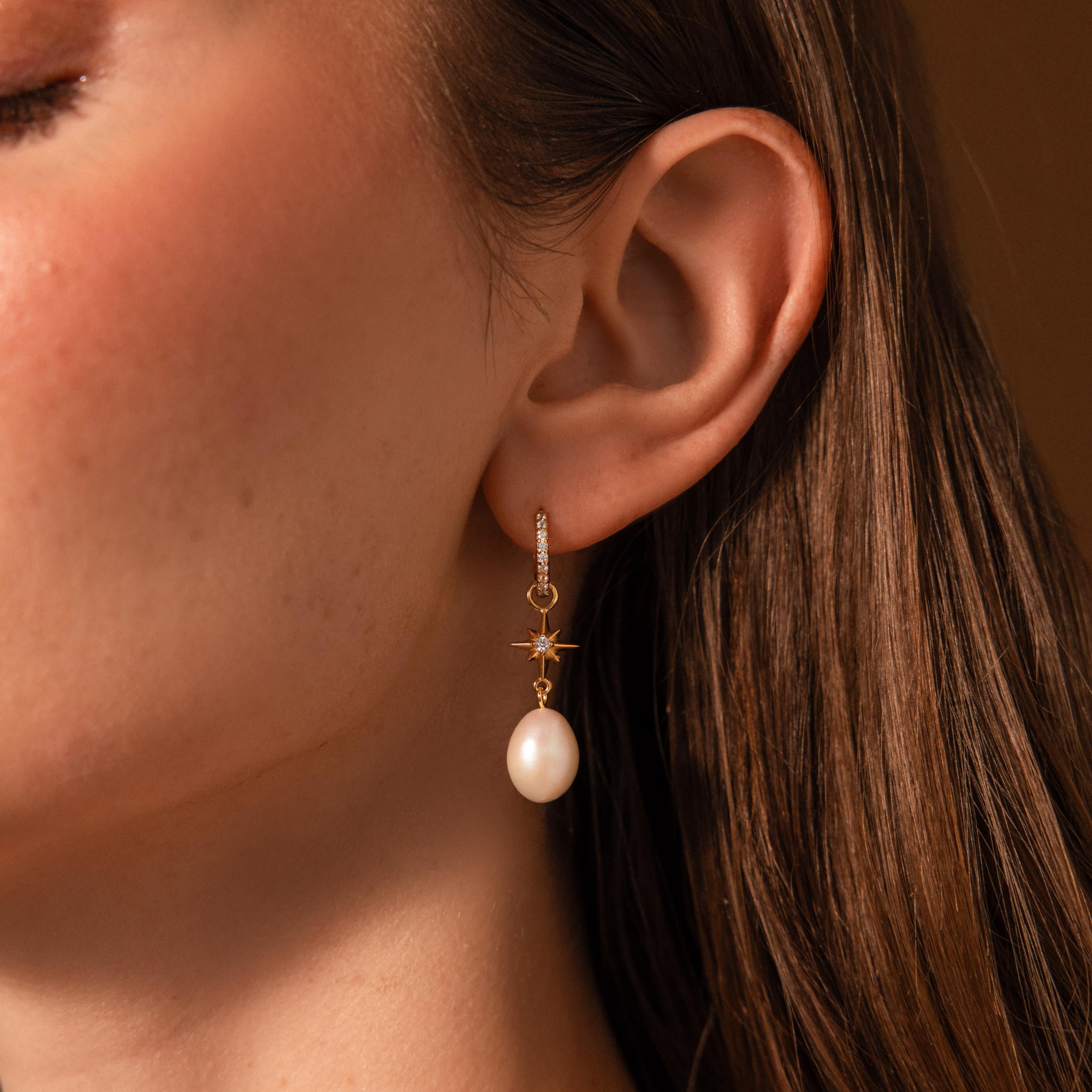 Close-up of a woman's ear wearing the North Star Pearl Hoops, gold earrings featuring a star charm and dangling white pearl.