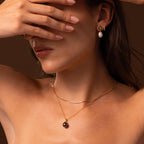 A woman covers her eyes against a brown background, wearing the Midnight Pearl Necklace. The elegant design and lustrous pearls capture the timeless allure of classic jewelry.