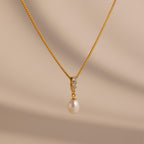 The Diamond Pearl Droplet Necklace features a gold drop design with a pearl pendant and small diamonds, shown against a light beige background—an elegant jewelry piece suitable for any occasion.