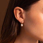 Close-up of a woman’s ear wearing Diamond Pearl Droplet Earrings embellished with small crystals.