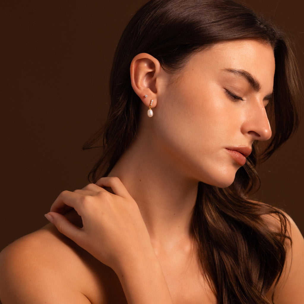 A woman with long brown hair wears Diamond Pearl Droplet Earrings, posing with her eyes closed against a brown background.