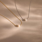 Two Tiny Pearl Dot Necklaces—one gold, one silver—each feature a simple pearl pendant and are displayed on a beige surface with soft shadows.