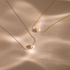 The Pearl Dot Necklace rests elegantly on a beige surface, its simple design highlighted by a delicate pearl accent.