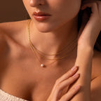 A woman wears a white strapless top paired with layered gold necklaces, featuring the Dainty Pearl Dot Necklace as a stunning pendant.