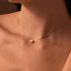 Close-up of a woman's neck wearing the Dainty Pearl Dot Necklace, featuring a delicate silver chain and a single white pearl pendant.