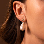 Close-up of a woman's ear wearing Diamond Baroque Pearl Studs, featuring a gold setting with a round diamond and an elegant, irregular baroque pearl drop.