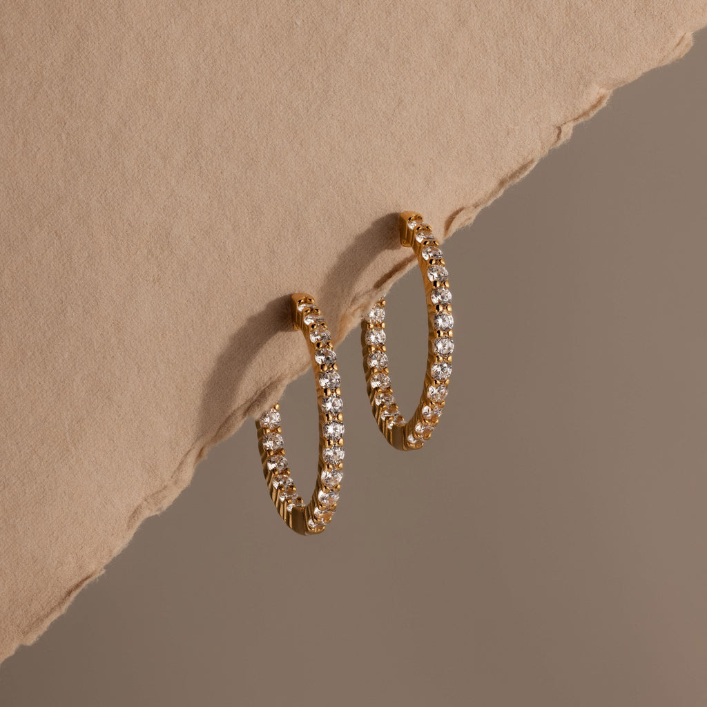 Inside Out Diamond Hoops in 18k gold with small diamonds, showcased on a textured beige surface and a soft brown backdrop.