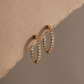 Inside Out Diamond Hoops in 18k gold with small diamonds, showcased on a textured beige surface and a soft brown backdrop.