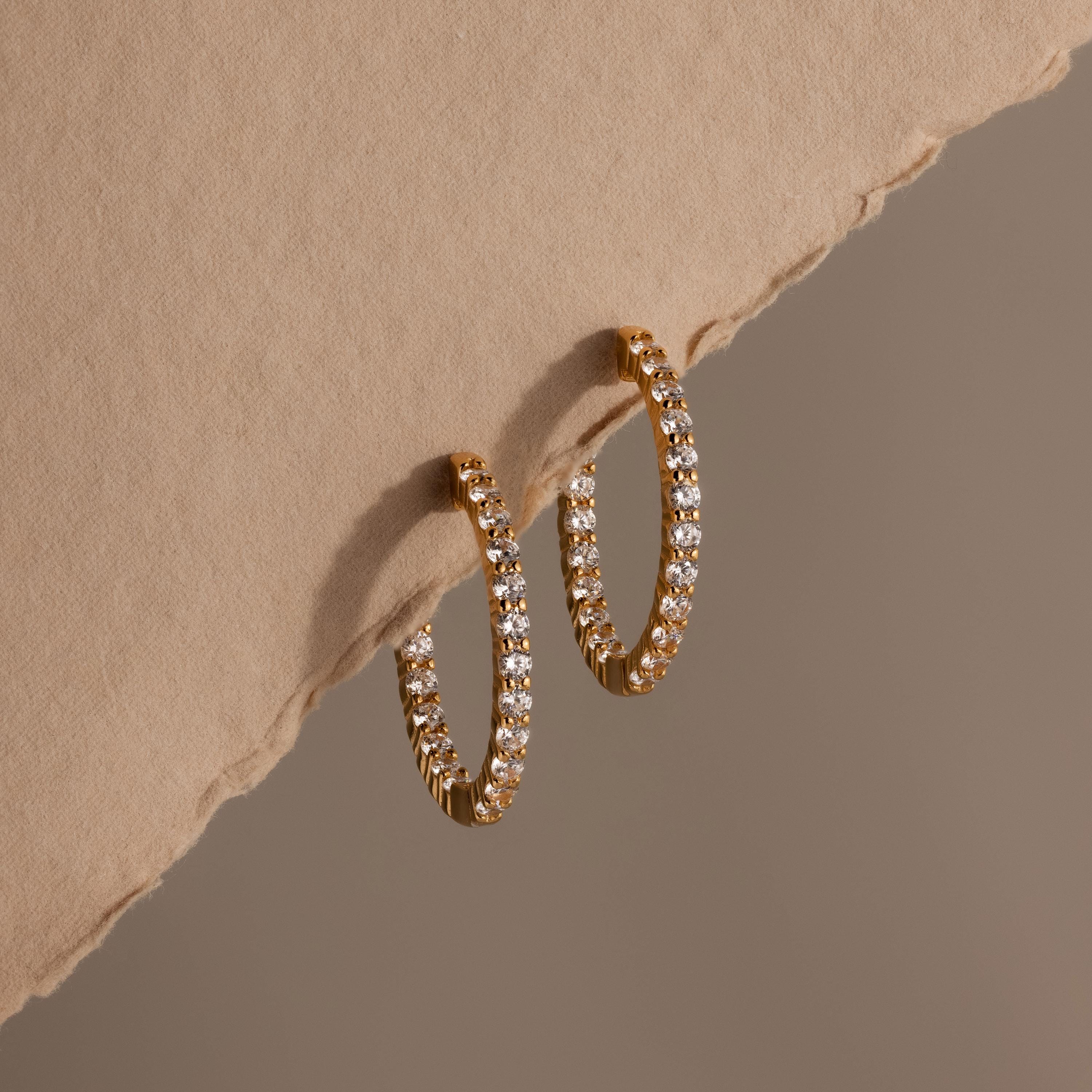Inside Out Diamond Hoops in 18k gold with small diamonds, showcased on a textured beige surface and a soft brown backdrop.