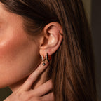 Close-up of a woman's ear wearing Noir Pave Dome Hoops in 18K Gold, accented with black enamel, with her hand gently touching her neck.