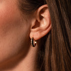 Close-up of a woman's ear wearing Noir Pave Dome Hoops in 18K Gold—glamorous gold hoops with sparkling stones and a sleek black enamel accent.