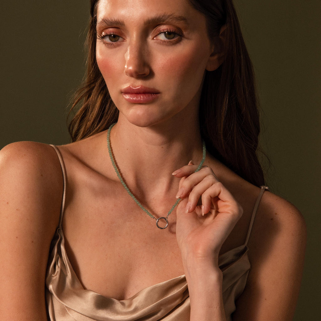 A woman poses for a photo, elegantly displaying the Beaded Jade Clasp Necklace in Silver, which adds a touch of sophistication to her look.