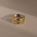 The Mixed Metal Linked Ring Set, crafted in gold and silver tones, rests on a smooth beige surface with a soft shadow—an elegant choice for those who appreciate meaningful jewelry.