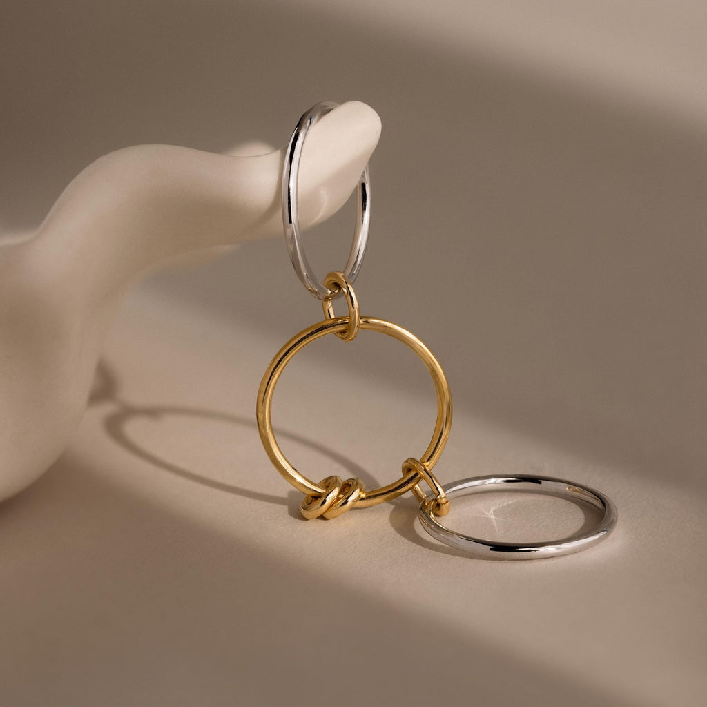 The Mixed Metal Linked Ring Set, featuring intertwined gold and silver hoops, is displayed on a smooth white sculptural hand.