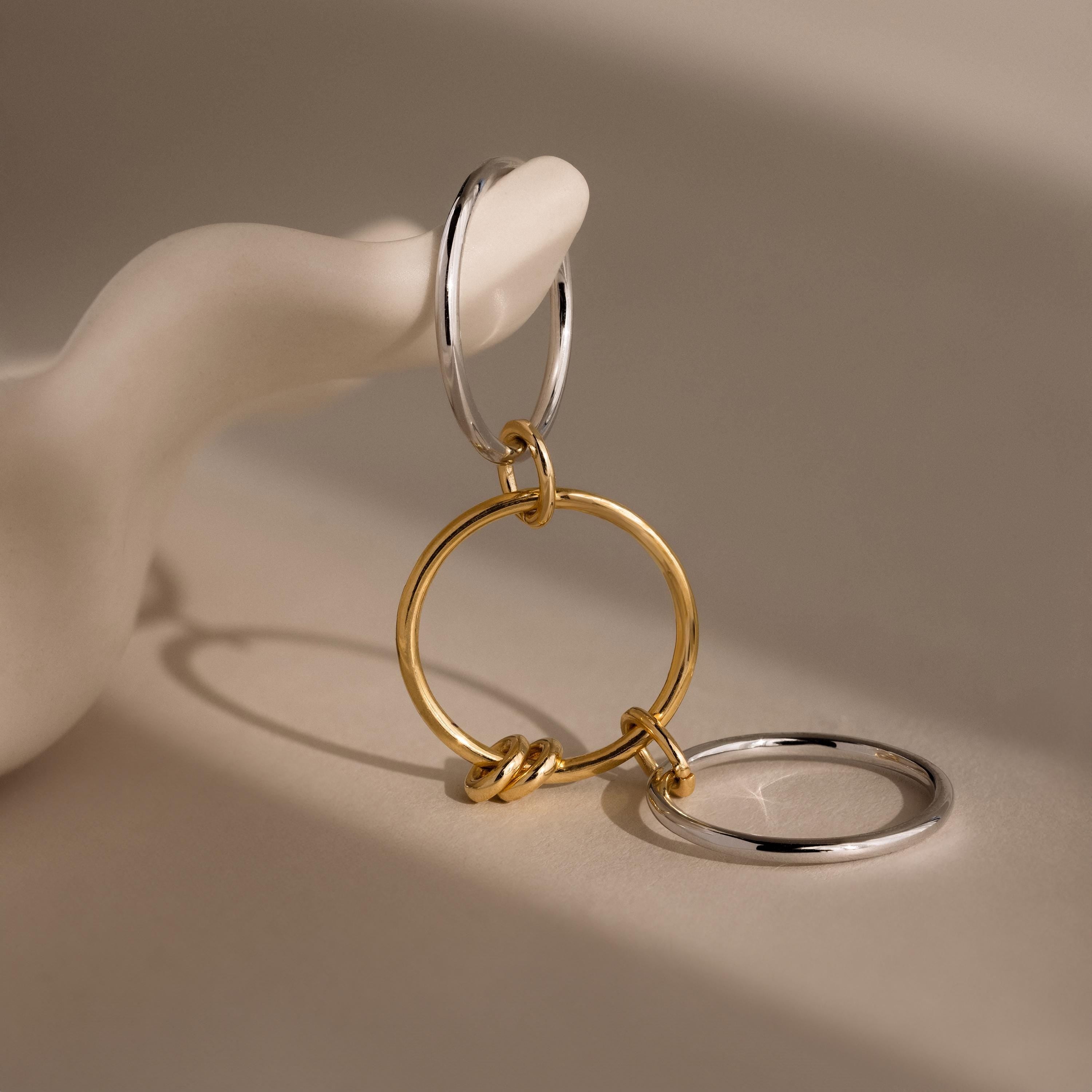 The Mixed Metal Linked Ring Set, featuring intertwined gold and silver hoops, is displayed on a smooth white sculptural hand.