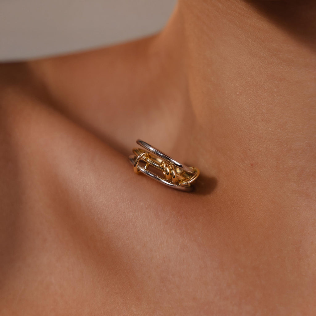 A close-up of the Mixed Metal Linked Ring Set in gold and silver rests on a person's collarbone, highlighting meaningful jewelry with subtle elegance.
