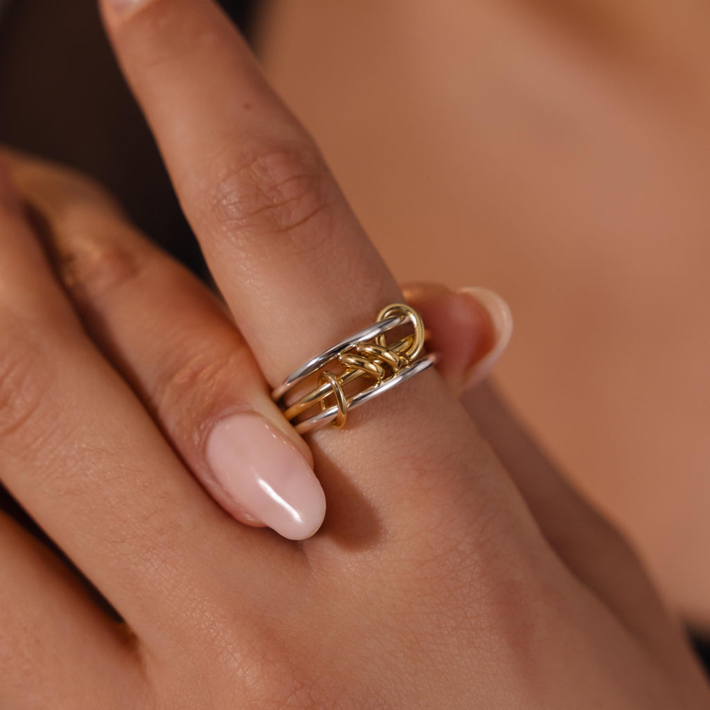 A hand with light pink nails wears the Mixed Metal Linked Ring Set on the middle finger, ideal for those who appreciate meaningful jewelry.