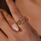 A hand with light pink nails wears the Mixed Metal Linked Ring Set on the middle finger, ideal for those who appreciate meaningful jewelry.