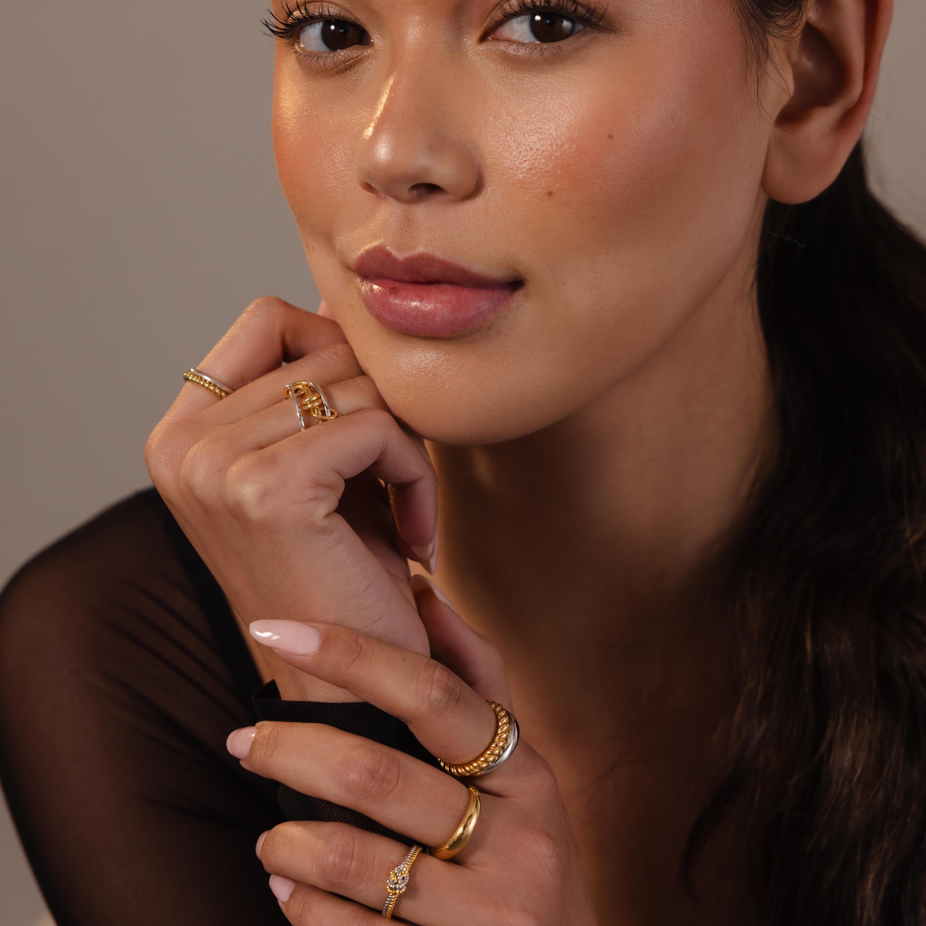 A woman with her hands under her chin showcases the Mixed Metal Linked Ring Set—meaningful jewelry that adds a touch of elegance.