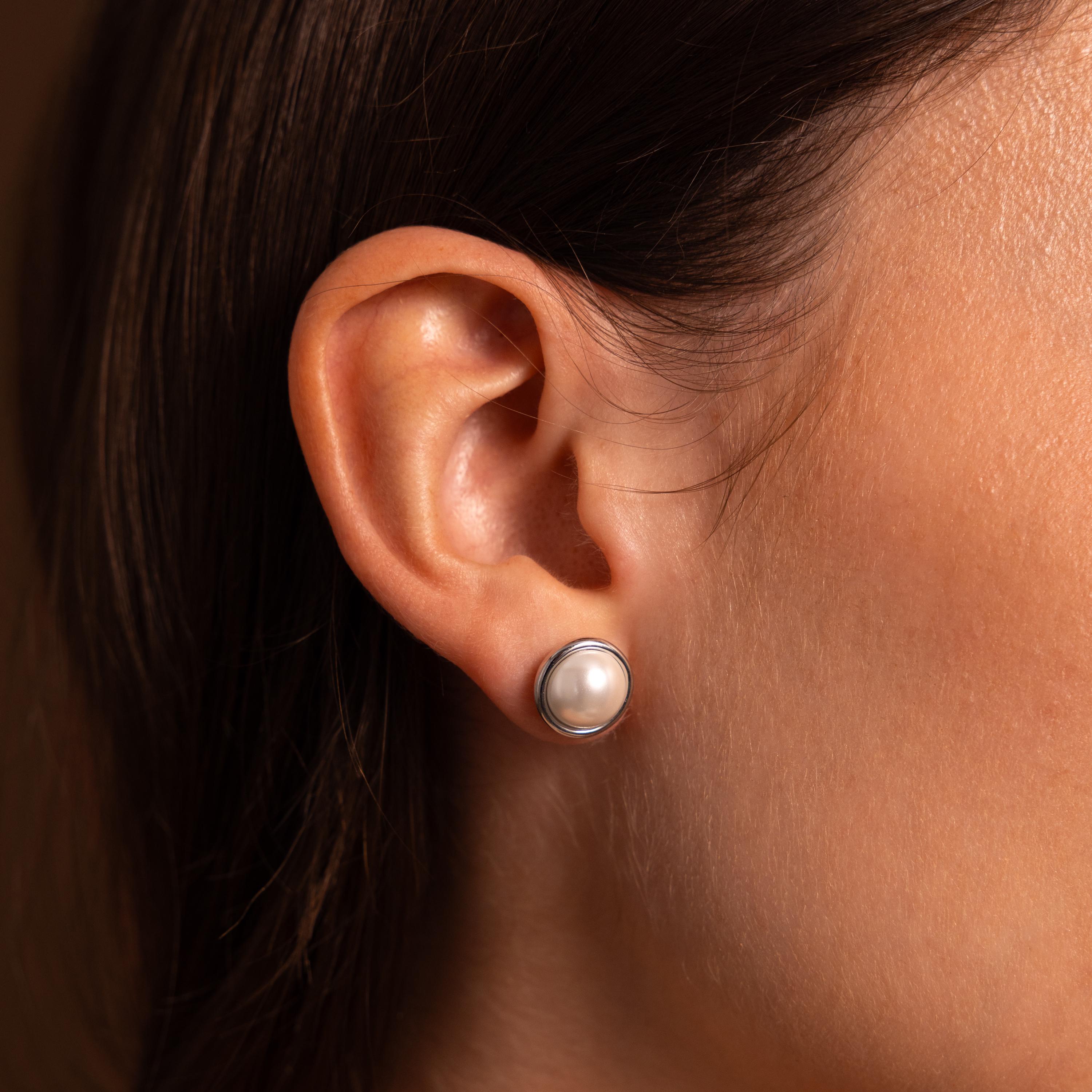 Close-up of a woman’s ear wearing Pearl Bezel Studs in Sterling Silver, highlighting the modern elegance of these round pearl earrings.