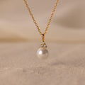 The Diamond Halo Pearl Necklace features a pearl pendant surrounded by small diamonds, elegantly showcased on a sandy surface—ideal for those who value timeless jewelry.