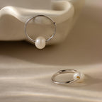 Two Round Pearl Hoops in Sterling Silver, each featuring a luminous pearl, are displayed on a soft beige surface.