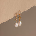North Star Pearl Hoops featuring elegant pearl drops and star details, showcased on a textured beige surface.