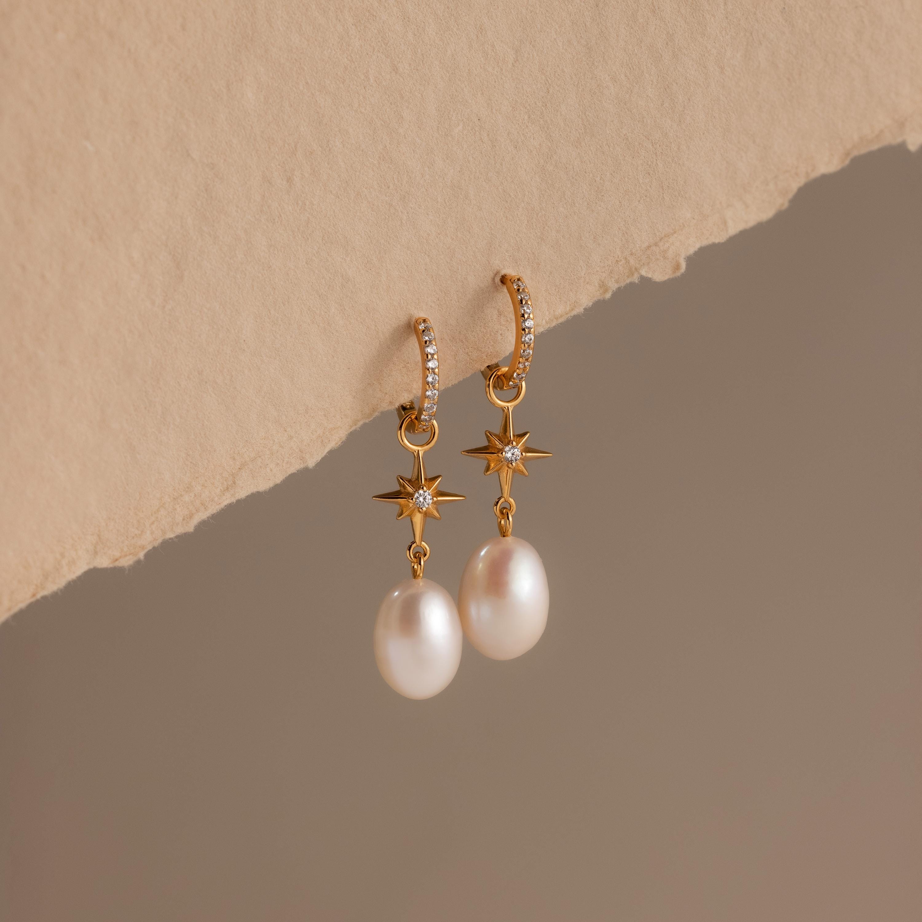 North Star Pearl Hoops featuring elegant pearl drops and star details, showcased on a textured beige surface.