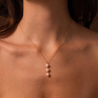 A woman wears the Pearl Cascade Necklace, showcasing three luminous pearls elegantly suspended against her skin.