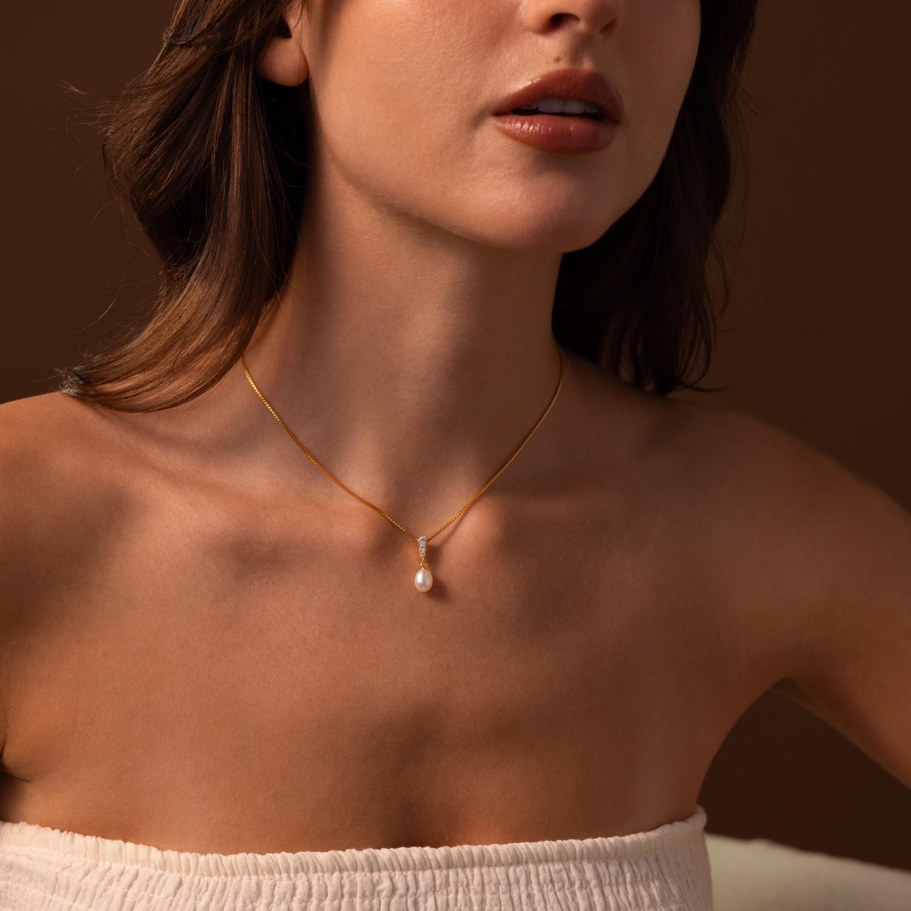 Woman wearing the Diamond Pearl Droplet Necklace in 18K Gold, featuring a delicate gold chain with a single pearl pendant, paired with a white off-shoulder top.
