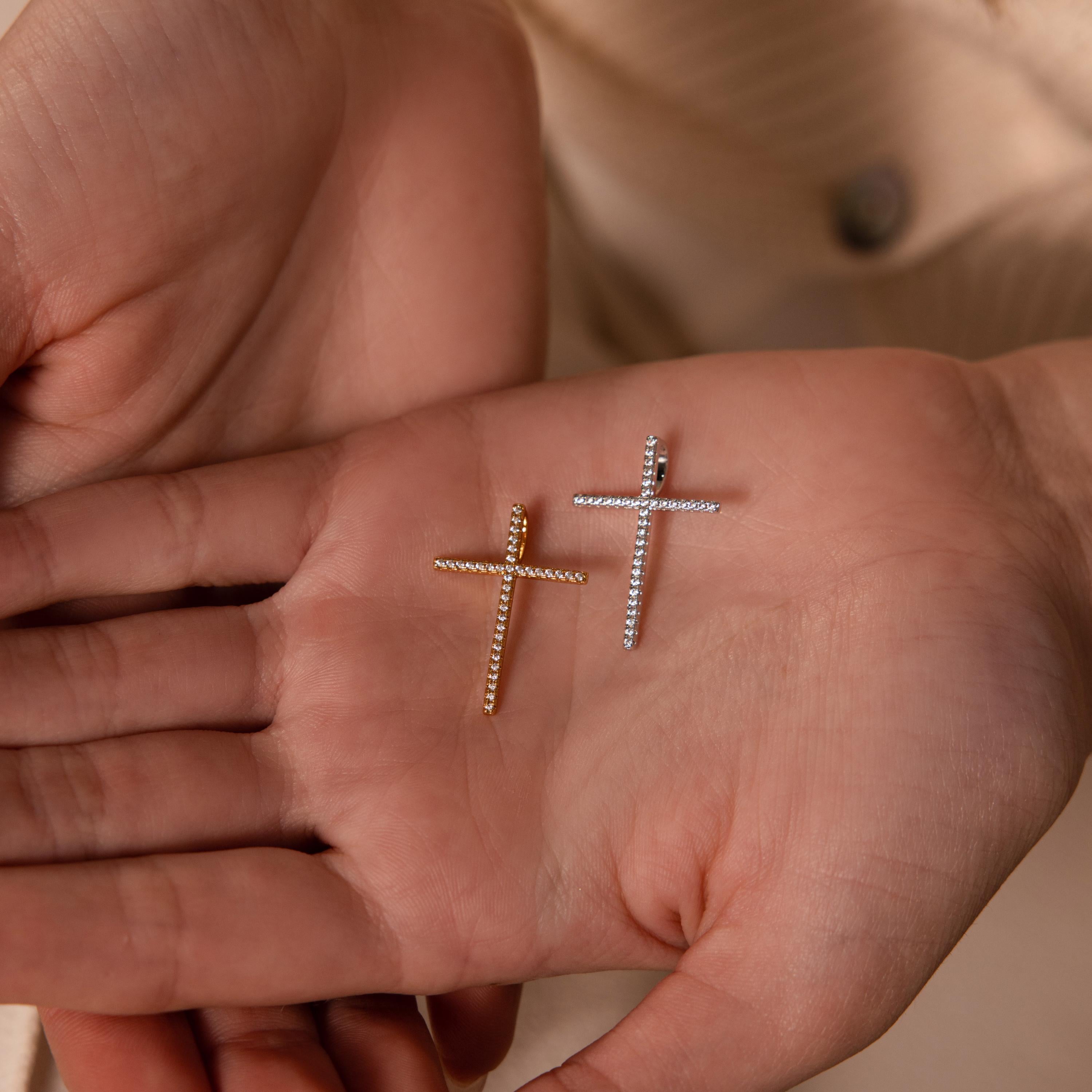 A hand elegantly holds the Skinny Pave Cross Charm in Silver, displayed prominently on an open palm.