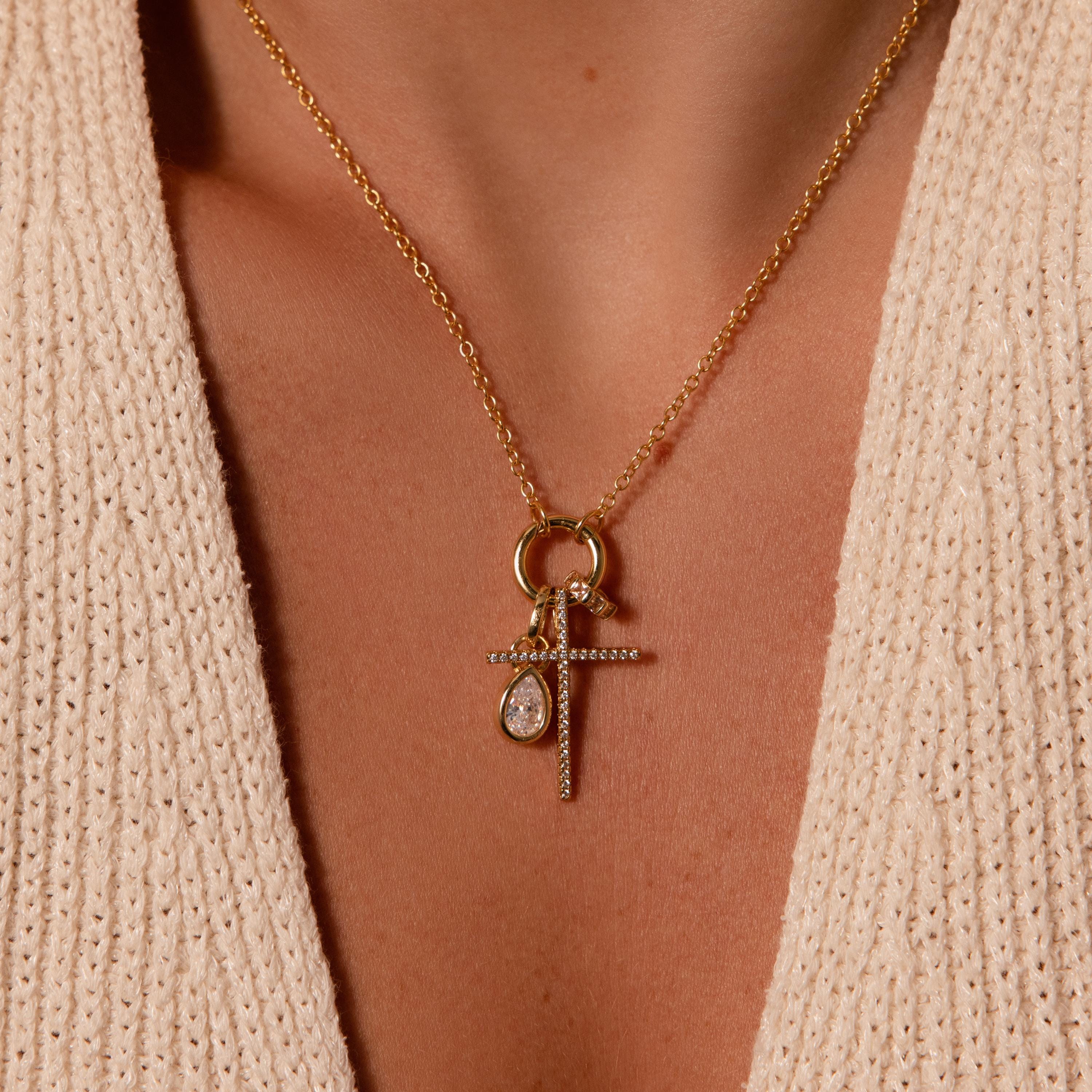 The Skinny Pave Cross Charm in 18K Gold, paired with a teardrop pendant, adds timeless elegance to a cream knit top with a deep neckline—a classic piece of faith jewelry.