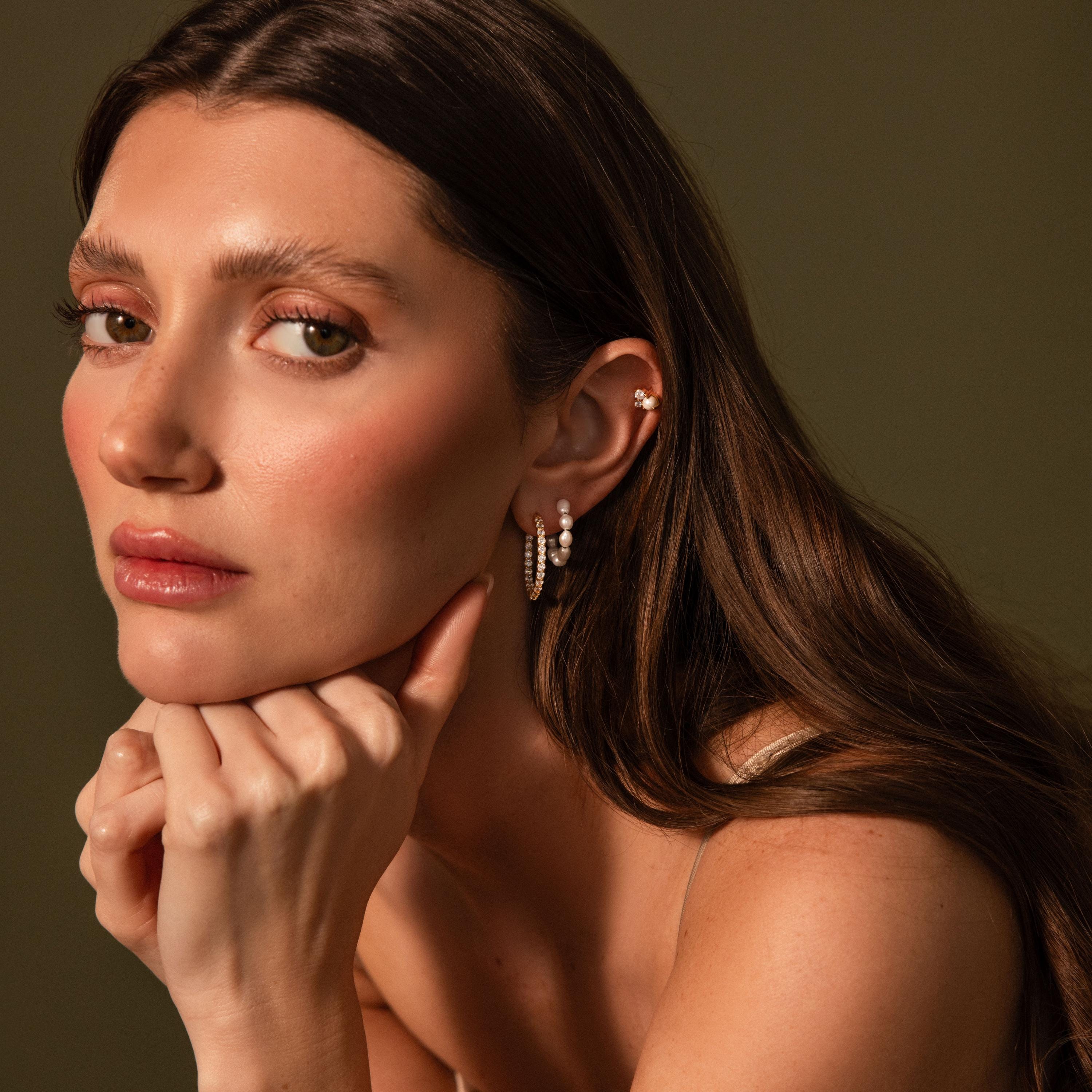 Woman with long brown hair, wearing Inside Out Diamond Hoops in 18K Gold, rests her chin on her hands and looks at the camera.