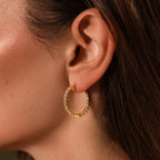 A woman’s ear is elegantly adorned with Inside Out Diamond Hoops, 18k gold hoops encrusted with sparkling gemstones.
