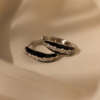 Noir Pave Dome Hoops featuring enamel black accents and clear gemstone pave, displayed on a soft beige fabric background.
