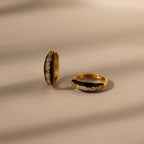 The Noir Pave Dome Hoops—gold hoop earrings featuring small diamonds and pave detailing—are displayed on a beige surface with soft shadow lines.