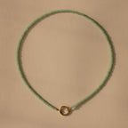 The Beaded Jade Clasp Necklace showcases smooth green jade beads and a small gold circular clasp, elegantly displayed on a beige background for a refined, sophisticated look.