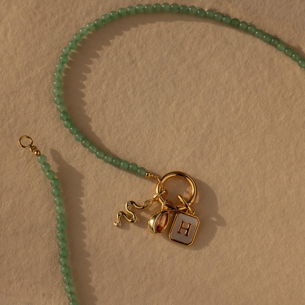 The Beaded Jade Clasp Necklace in 18K Gold features green jade beads and gold snake, bell, and “H” square charms. Finished with a gold clasp, it’s perfect for chic layering.