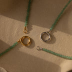 Two Beaded Jade Clasp Necklaces are displayed on a textured beige surface in sunlight, showing off their elegant gold and silver clasps.