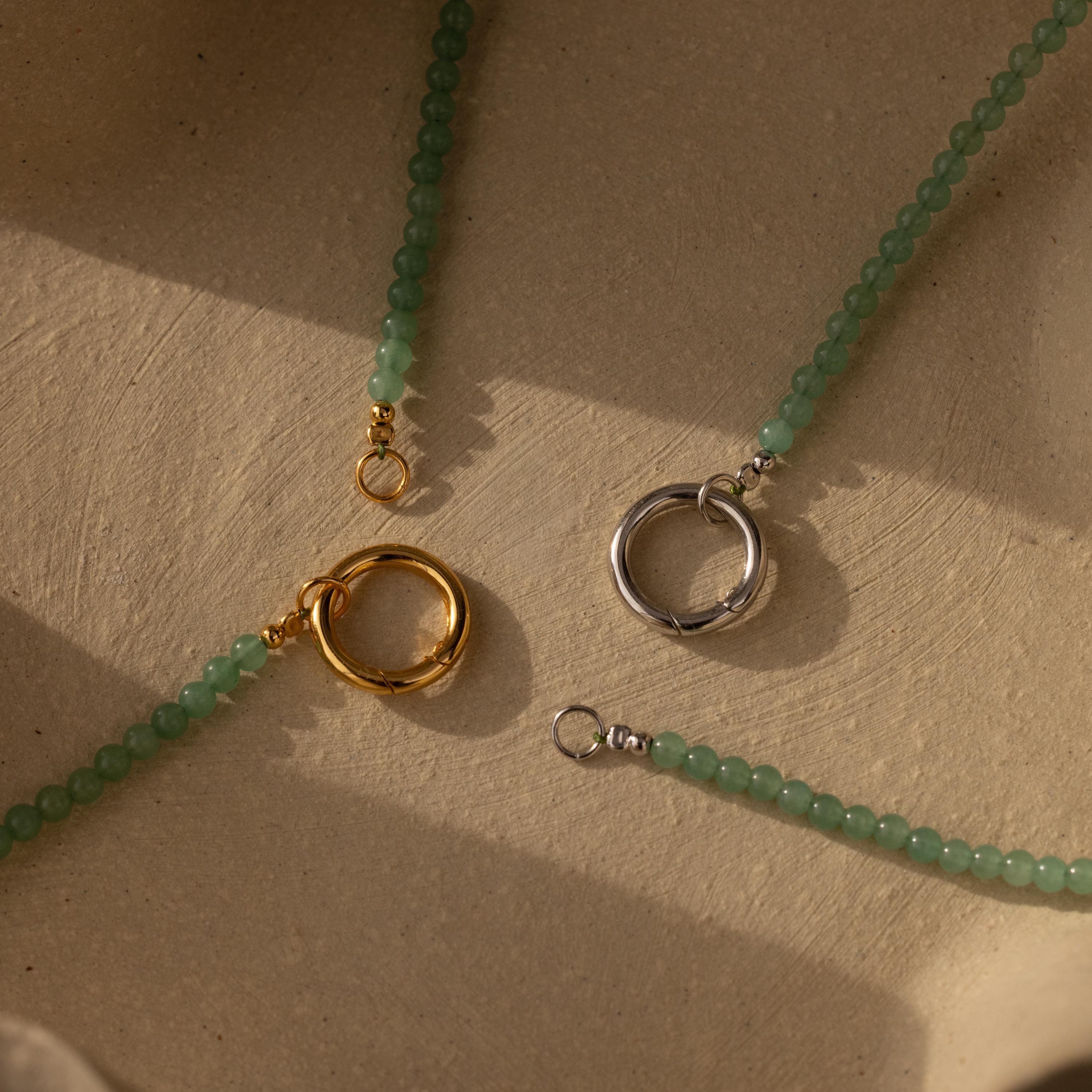 Two Beaded Jade Clasp Necklaces are displayed on a textured beige surface in sunlight, showing off their elegant gold and silver clasps.