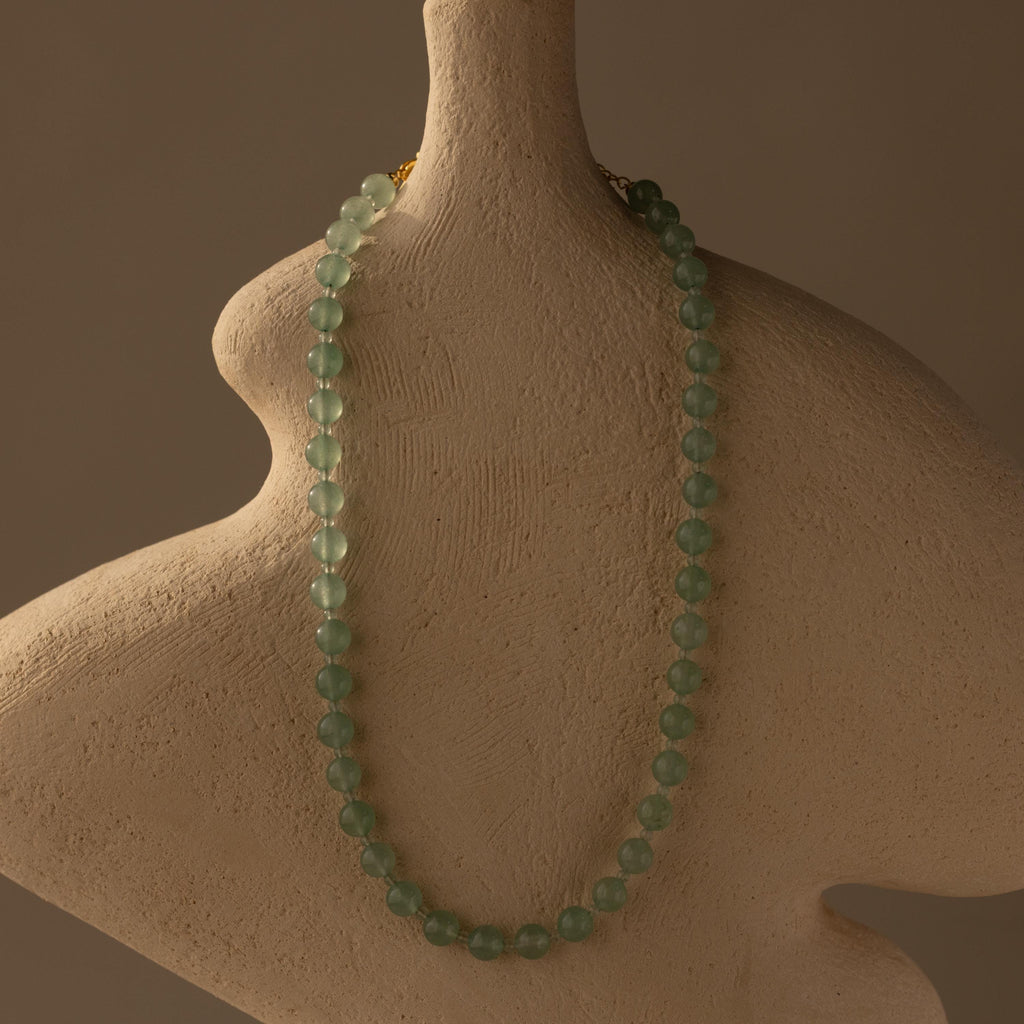 The Jade Choker Necklace with green beads is shown on a textured, abstract beige bust set against a neutral background.
