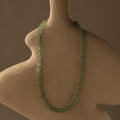 The Jade Choker Necklace with green beads is shown on a textured, abstract beige bust set against a neutral background.
