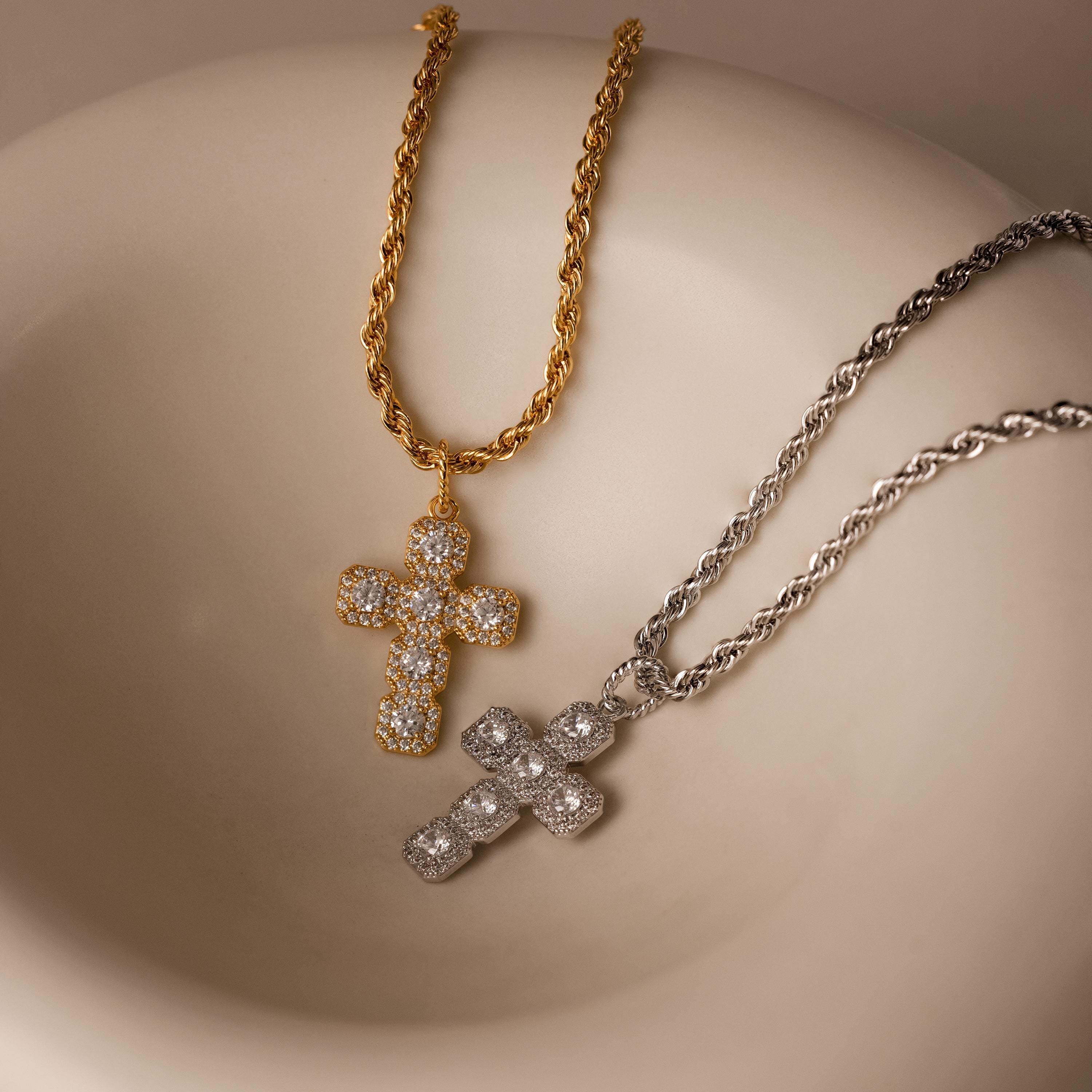 The Majesty Cross Necklace, adorned with diamonds in gold and silver finishes, is the perfect piece of faith jewelry, elegantly displayed on a smooth, light-colored surface.