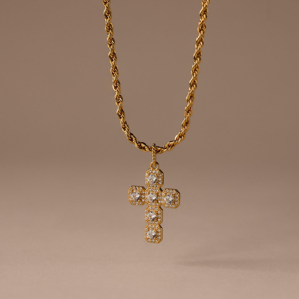 The Majesty Cross Necklace in 18K Gold features a diamond-studded cross pendant on a gold rope chain, ideal as faith jewelry, shown against a neutral brown background.