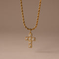 The Majesty Cross Necklace in 18K Gold features a diamond-studded cross pendant on a gold rope chain, ideal as faith jewelry, shown against a neutral brown background.