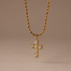 The Majesty Cross Necklace in 18K Gold features a diamond-studded cross pendant on a gold rope chain, ideal as faith jewelry, shown against a neutral brown background.