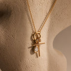 The Skinny Pave Cross Charm in 18K Gold, paired with a teardrop gemstone pendant and displayed on a beige sculpted mannequin, is perfect for those seeking elegant faith jewelry.